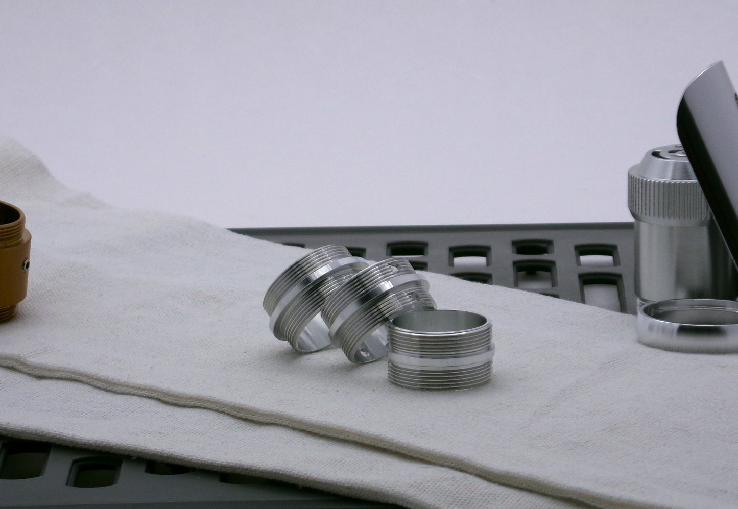 A trio of aluminum Male/Male threaded adapters in varying diameters, for VHC lightsabers; resting askew.