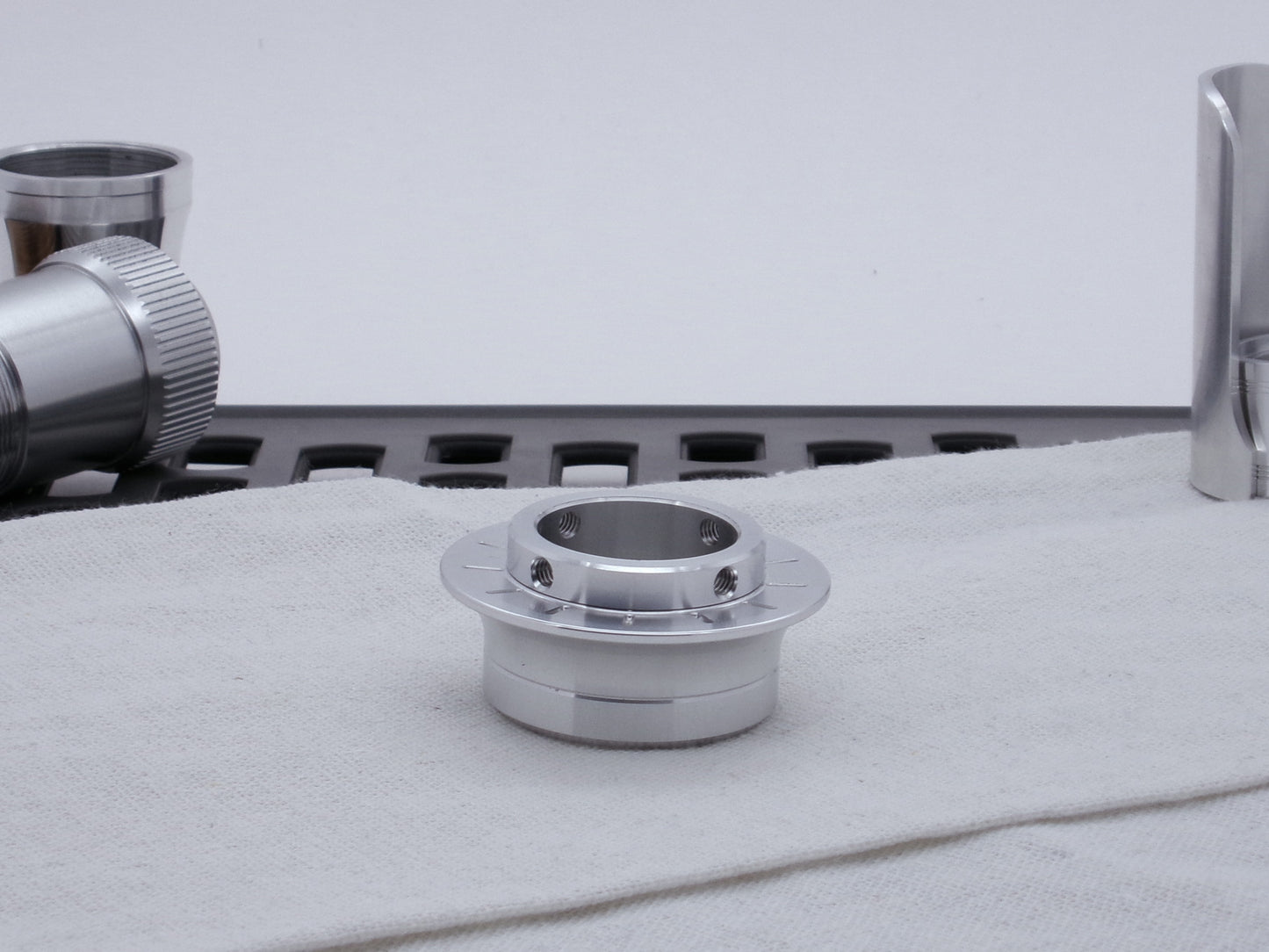 A VHC compatible lightsaber Emitter Flange threaded to an Emitter Tip, resting on cloth among lightsaber parts.