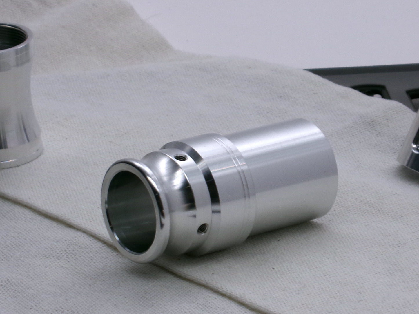 An aluminum, VHC compatible emitter tip installed on several lightsaber components, 3/4 view on a coarse cloth.