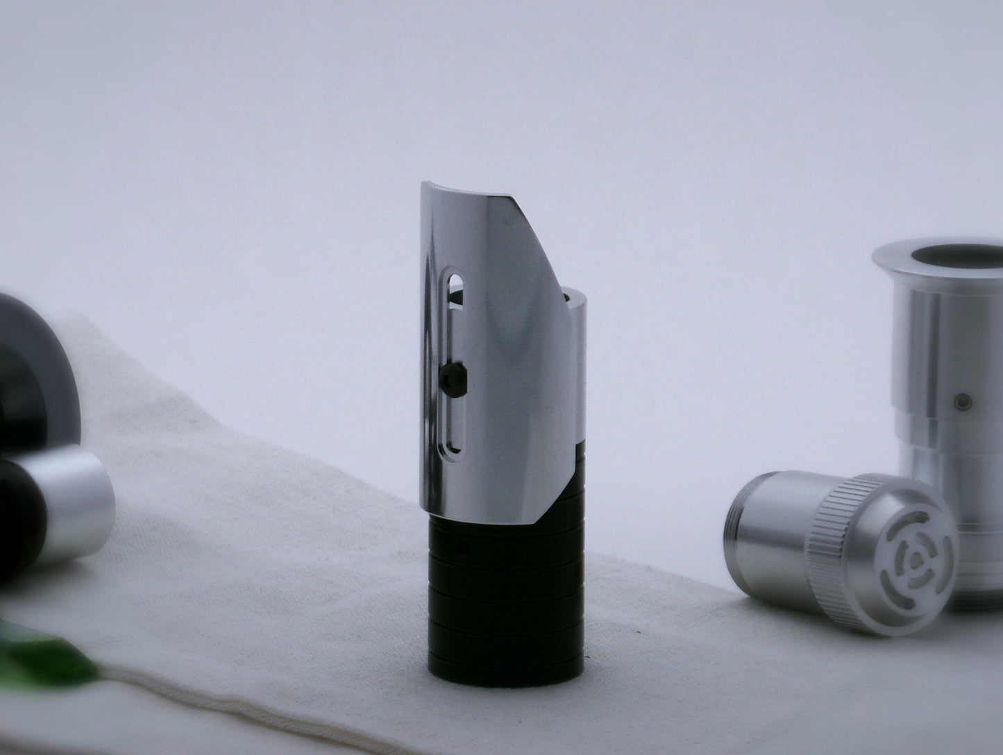 Small, shield shaped, aluminum half shroud for VHC lightsabers with angled ends mounted by universal slot to an emitter mock-up; vertically oriented, posterior view.