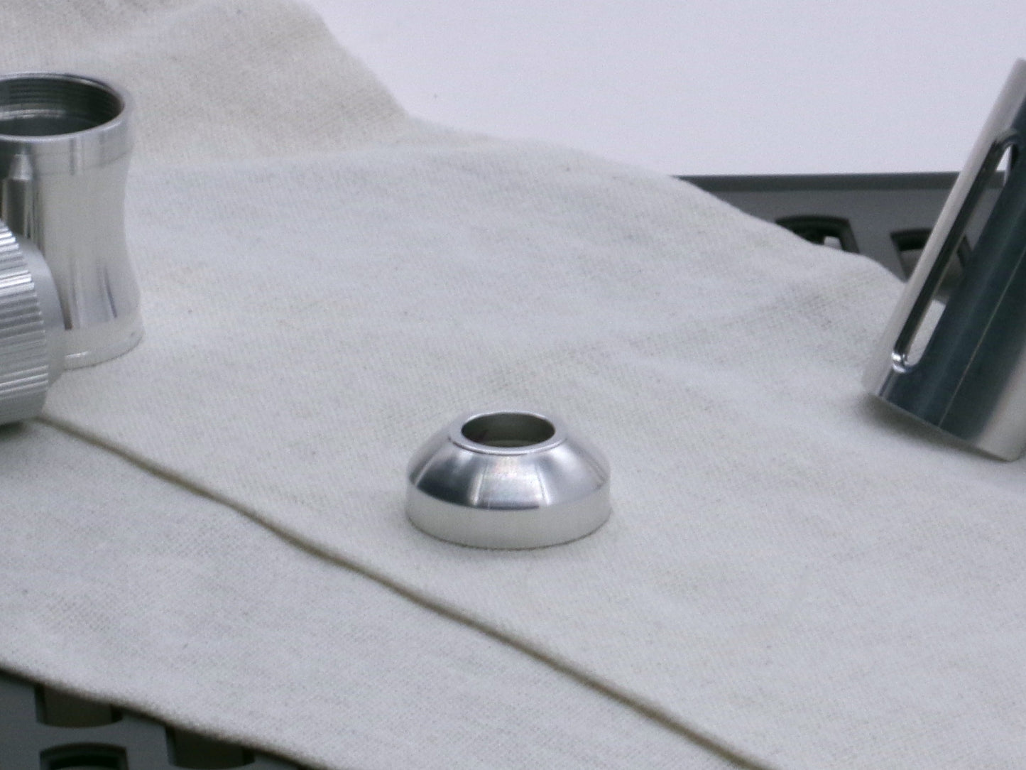A basic, aluminum female-threaded pommel. Shows rounded profile and single sound exit hole lying flat.