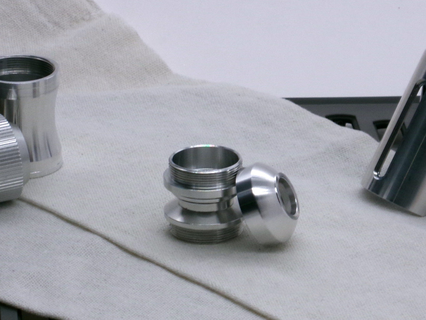 A basic, aluminum female-threaded pommel leaning against the Adapter MM Hybrid Type 1 showing rounded profile and sound aperture.