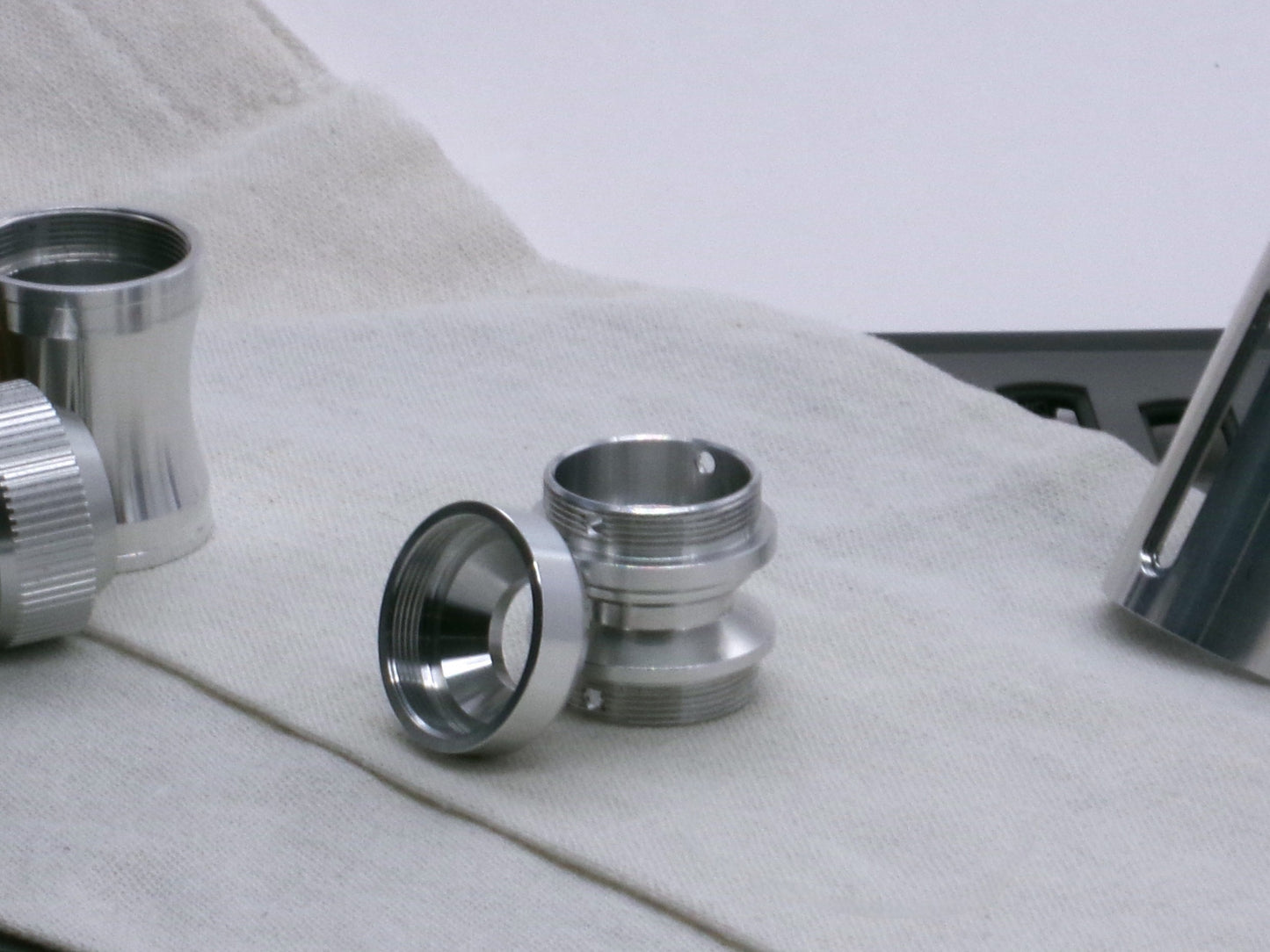 A basic, aluminum female-threaded pommel leaning against the Adapter MM Hybrid Type 1 showing internal chamfer profile and sound aperture.