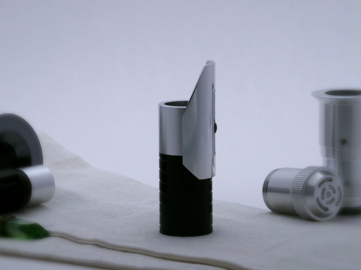 Small, shield shaped, aluminum half shroud for VHC lightsabers with angled ends mounted by universal slot to an emitter mock-up; vertically oriented, lateral view.