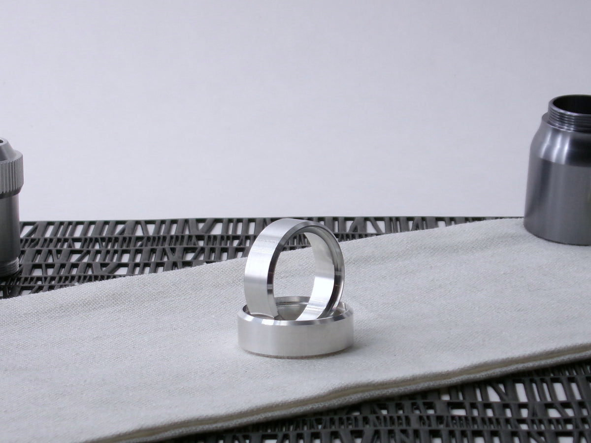 A pair of VHC compatible lightsaber parts, accent bands one supporting the other on cloth.