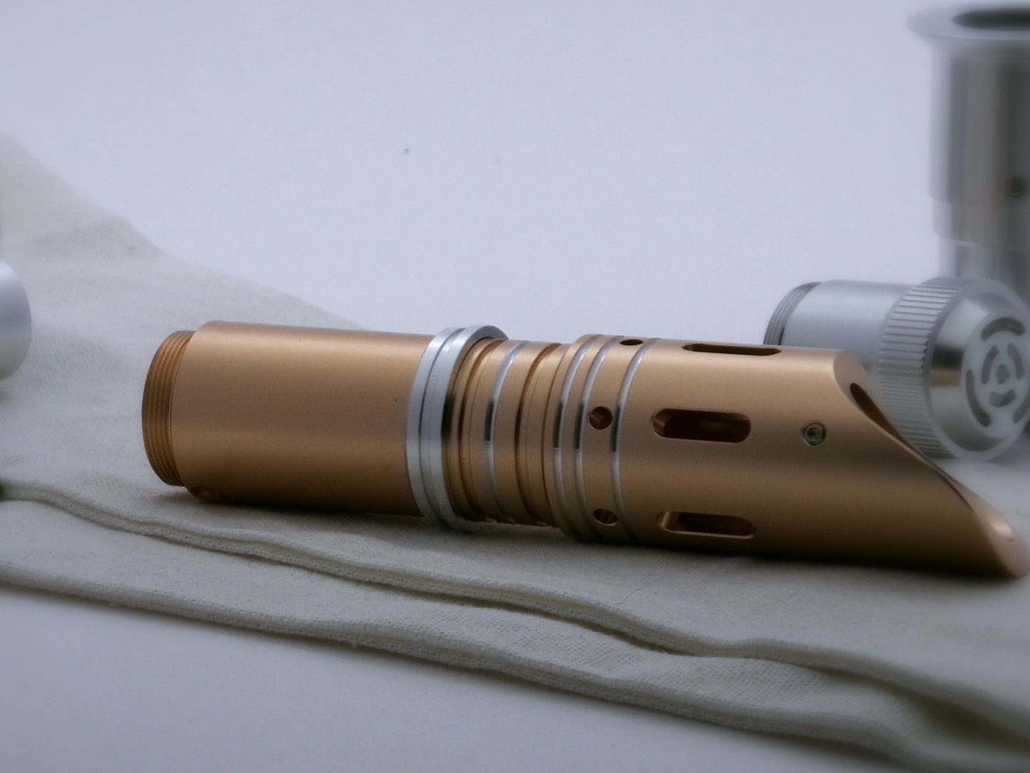 Single, aluminum accent ring with offset bands and a deep central groove installed between the switch and emitter of a golden VHC lightsaber.