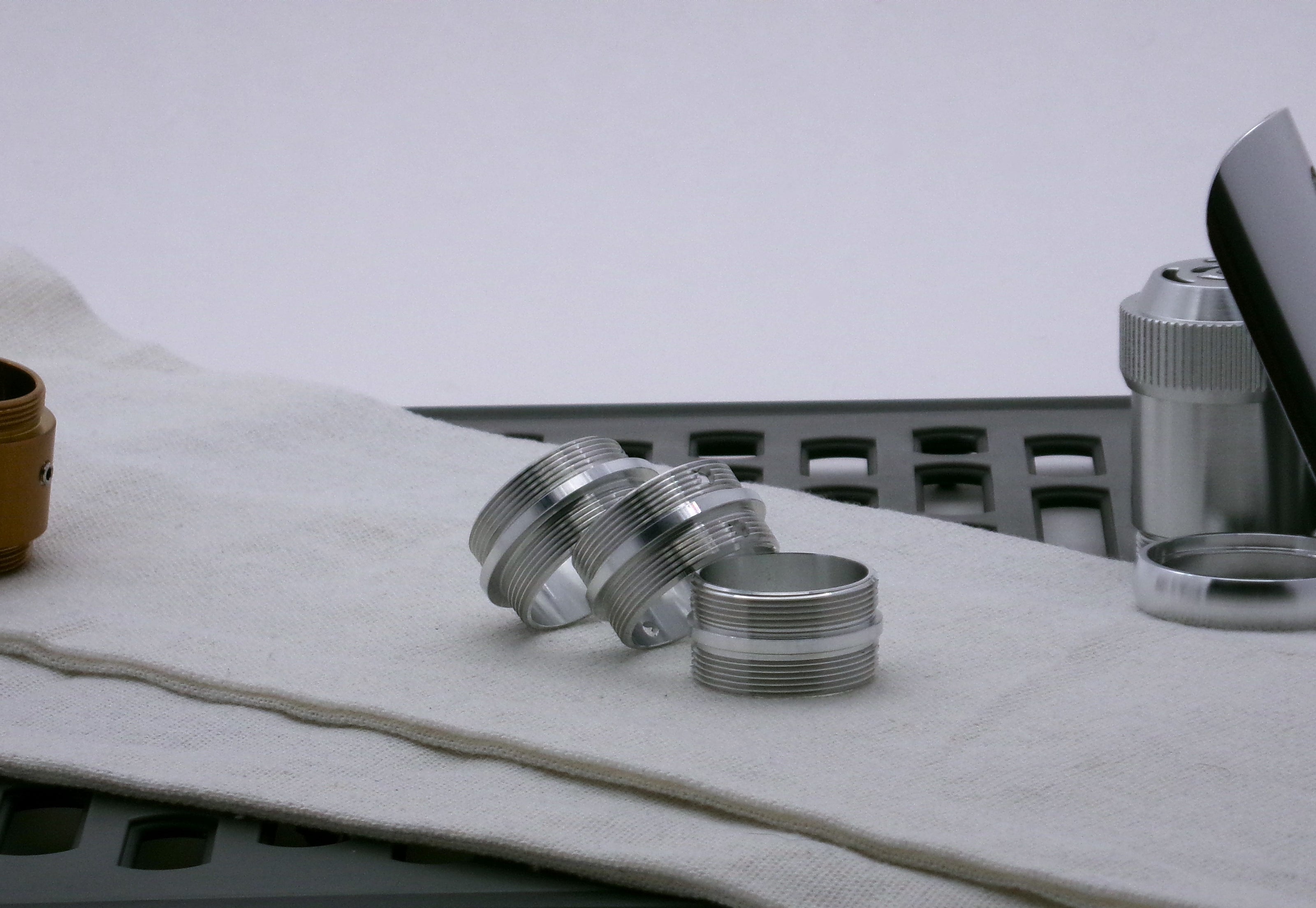 A trio of aluminum Male/Male threaded adapters in varying diameters, for VHC lightsabers; resting askew. 