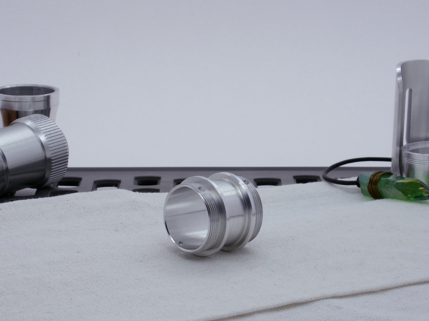 Male threaded VHC compatible lightsaber adapter resting on cloth, three-quarter view angled left.