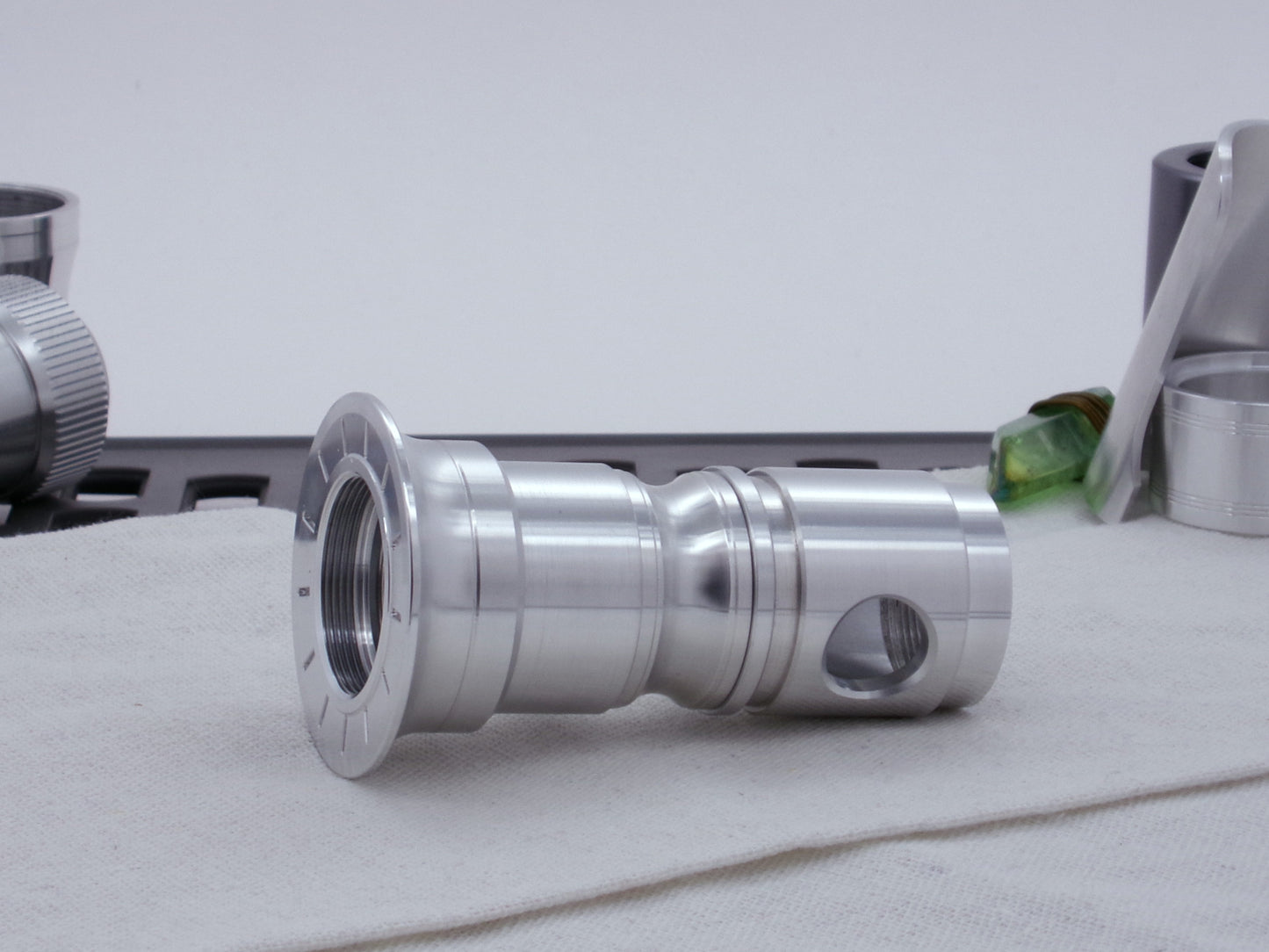 Male threaded, round choke for VHC lightsabers installed as part of an emitter assembly.  Resting on cloth, three-quarter view angled left.