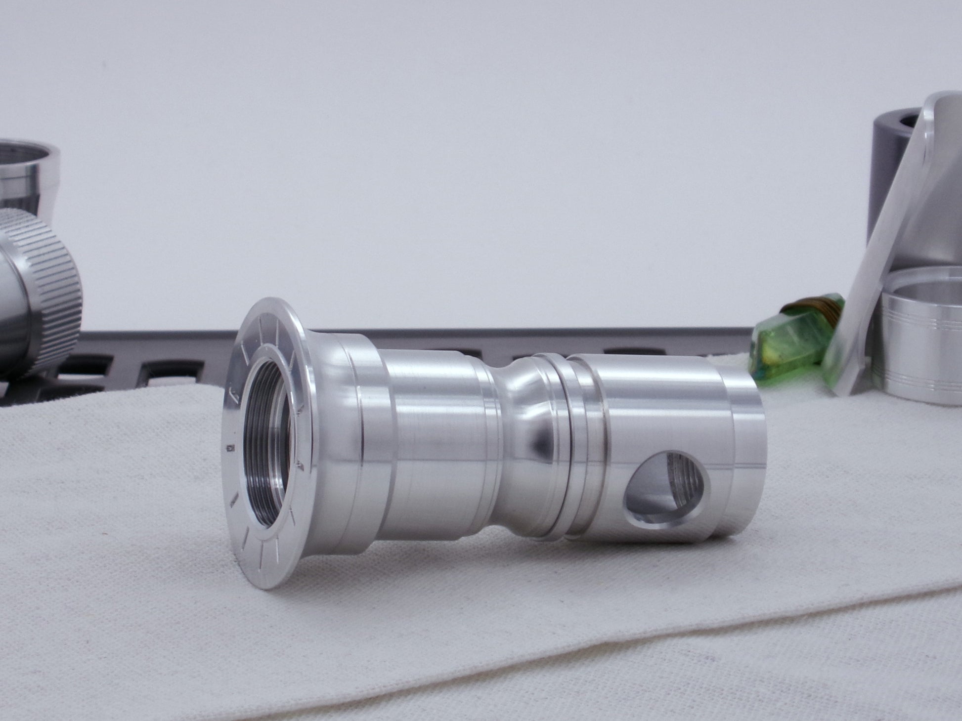 Male threaded, round choke for VHC lightsabers installed as part of an emitter assembly.  Resting on cloth, three-quarter view angled left.
