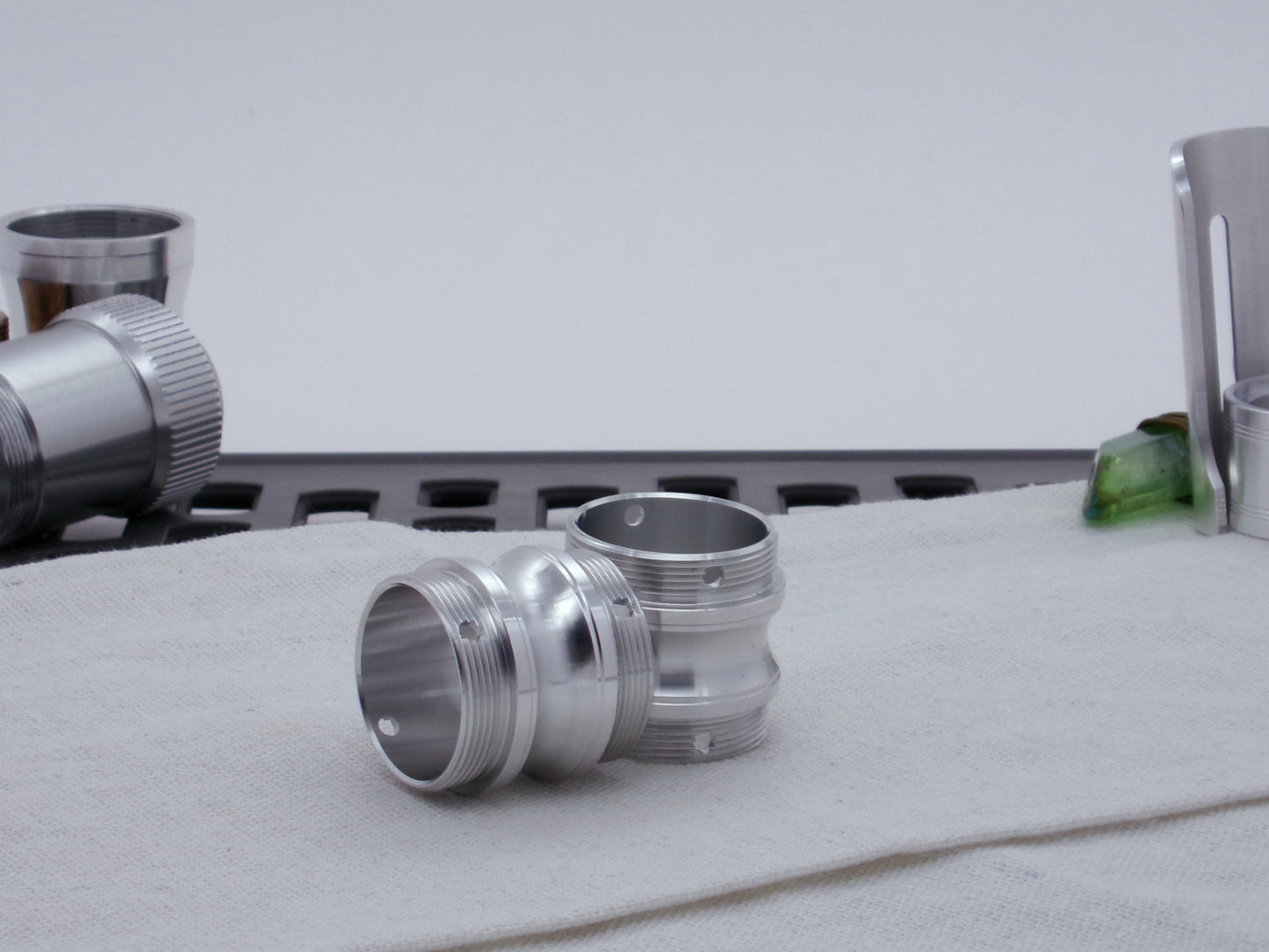 Pair of male threaded, round choke adapters for VHC lightsabers, resting on cloth askew among other saber components.