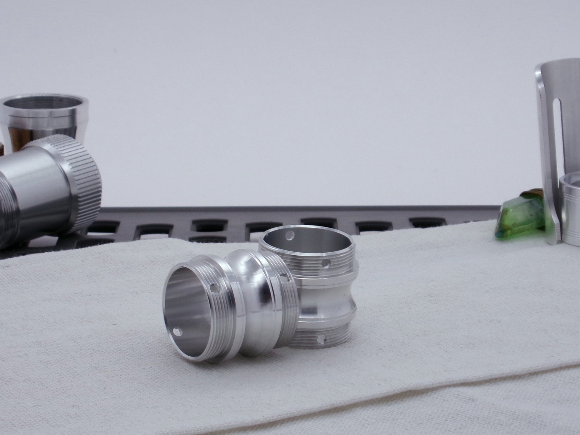 Pair of male threaded, round choke adapters for VHC lightsabers, resting on cloth askew among other saber components.