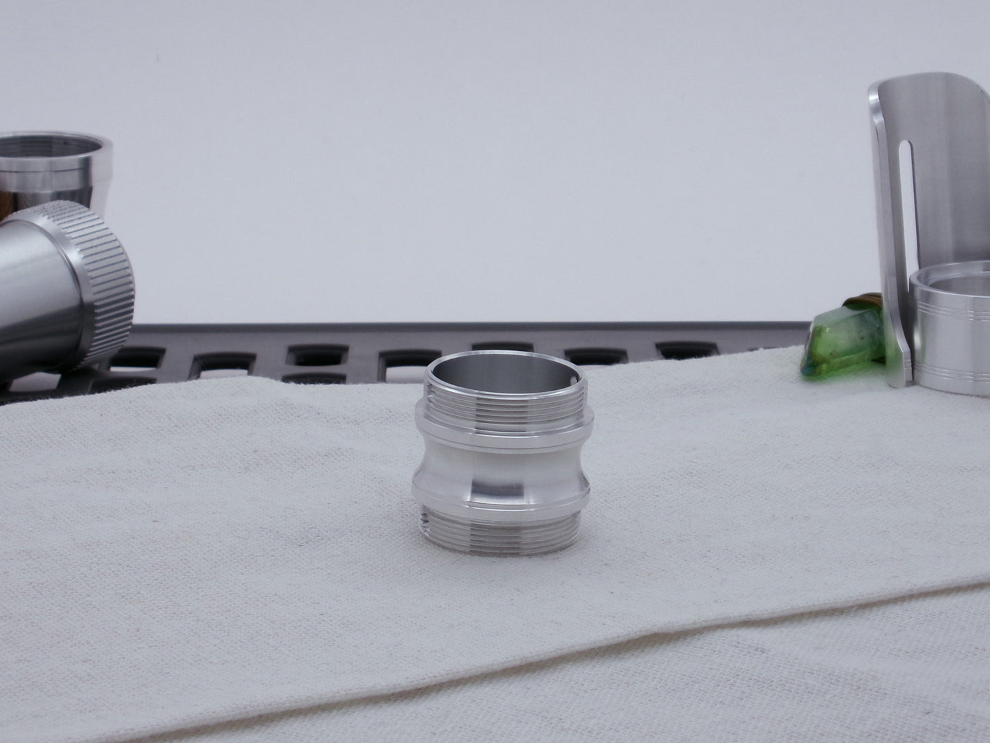 Male threaded, round choke adapter for VHC lightsabers, resting vertically on cloth among other parts.