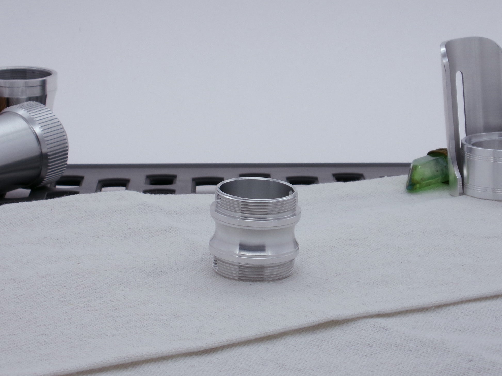 Male threaded, round choke adapter for VHC lightsabers, resting vertically on cloth among other parts.