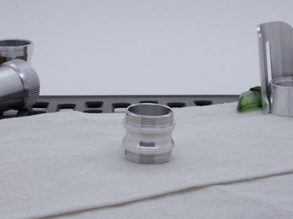 Male threaded, round choke adapter for VHC lightsabers, resting vertically on cloth among other parts.