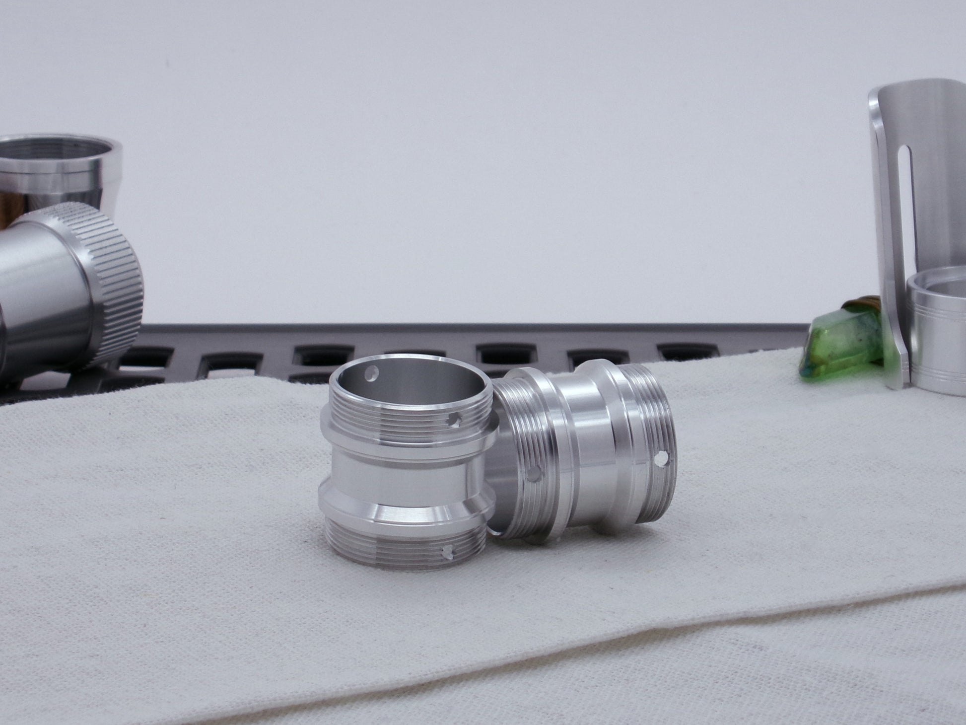 Pair of male threaded, angled choke adapters with for VHC lightsabers resting askew on cloth among other components.