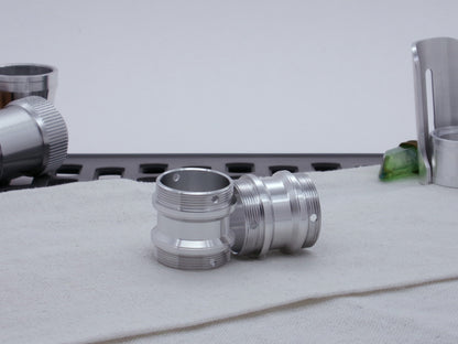 Pair of male threaded, angled choke adapters with for VHC lightsabers resting askew on cloth among other components.