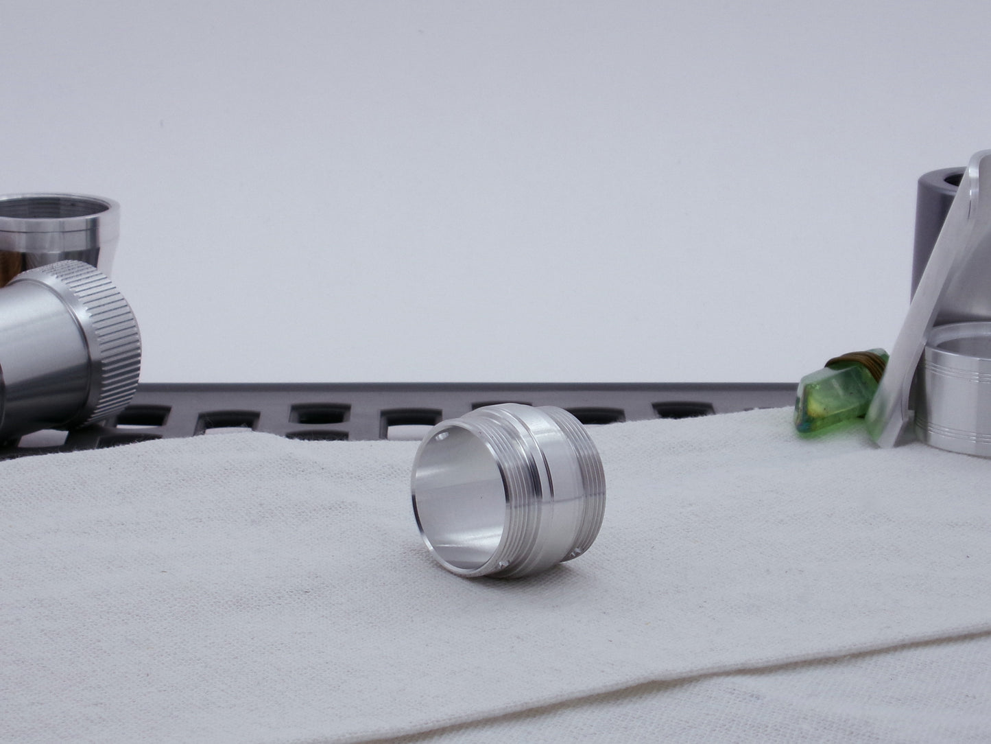 Ki Adi Mundi styled, stepped, male threaded adapter for VHC lightsabers resting on cloth, three-quarter view among other saber parts.