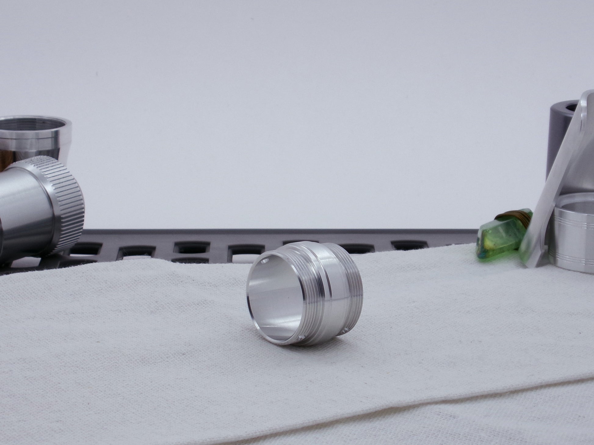 Ki Adi Mundi styled, stepped, male threaded adapter for VHC lightsabers resting on cloth, three-quarter view among other saber parts.