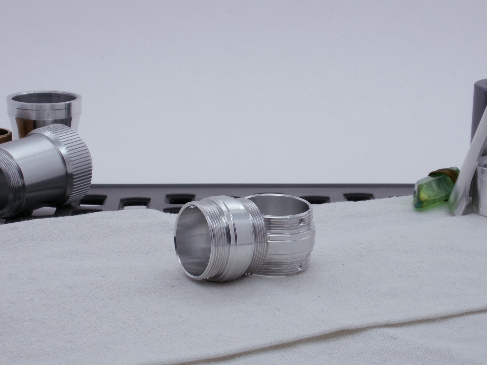 Ki Adi Mundi styled pair of stepped, male threaded adapters for VHC lightsabers, resting askew on cloth among other lightsaber parts.