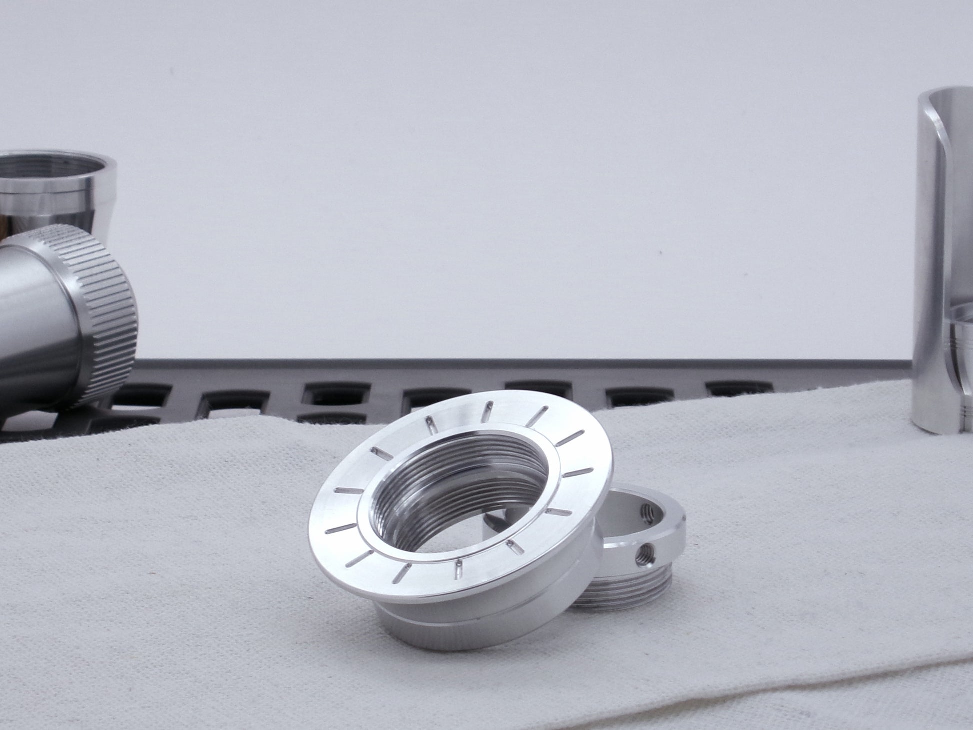 A VHC compatible lightsaber Emitter Flange askew atop an Emitter Tip, resting on cloth among lightsaber parts.