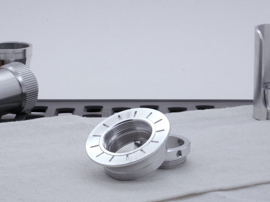 A VHC compatible lightsaber Emitter Flange askew atop an Emitter Tip, resting on cloth among lightsaber parts.