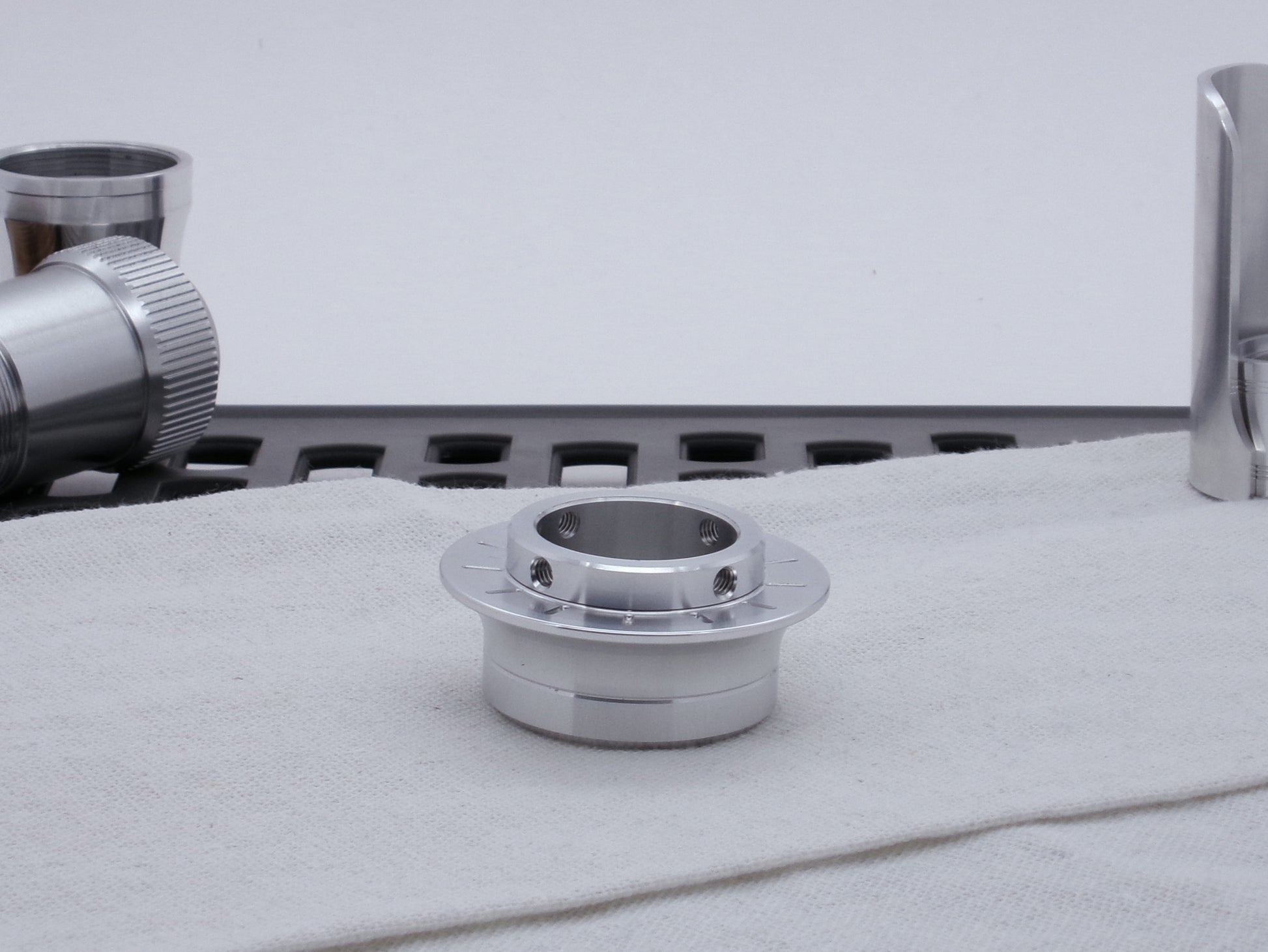 A VHC compatible lightsaber Emitter Flange threaded to an Emitter Tip, resting on cloth among lightsaber parts.