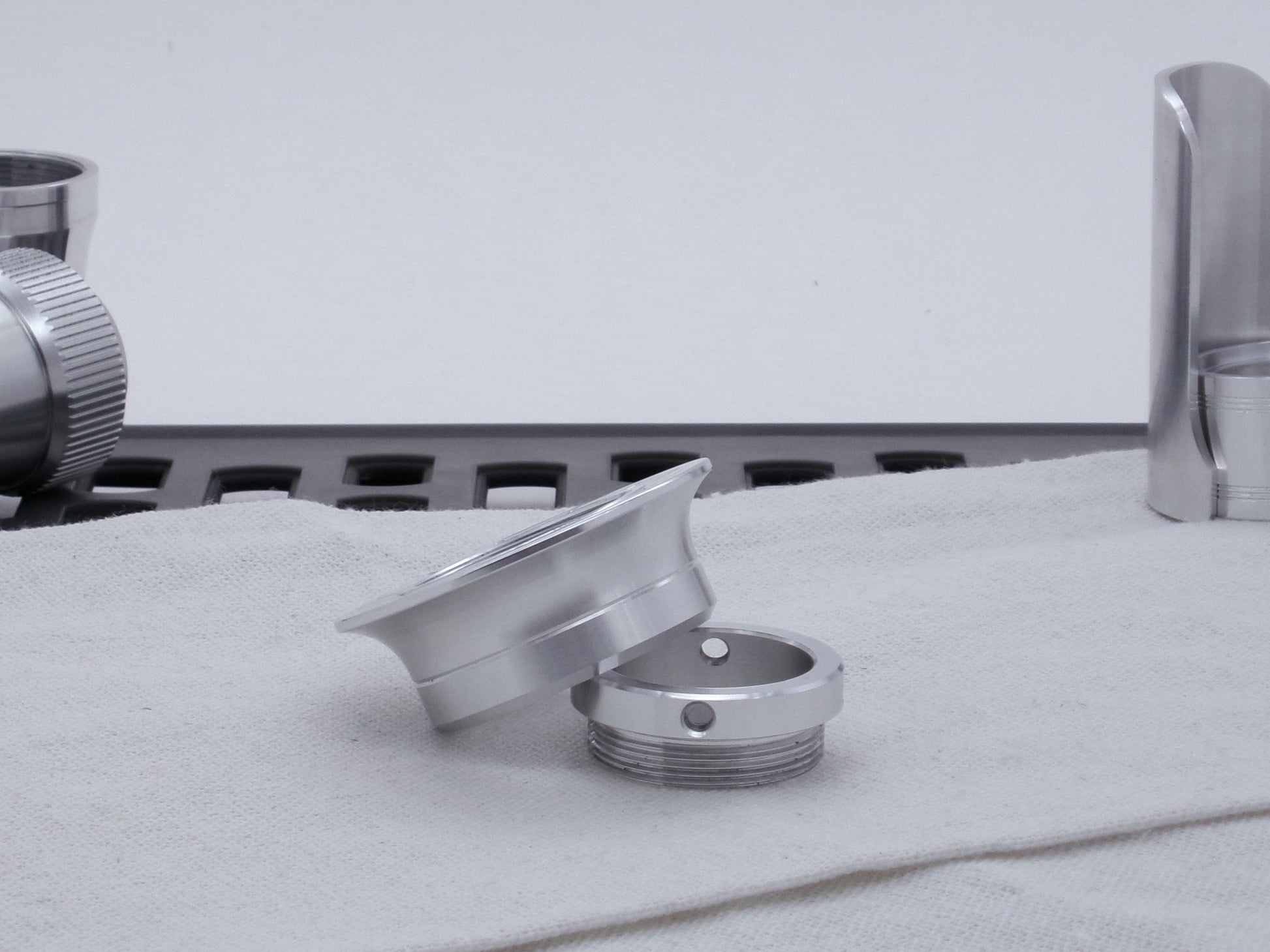 A VHC compatible lightsaber Emitter Flange askew atop an Emitter Tip in profile, resting on cloth among lightsaber parts.