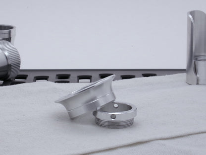 A VHC compatible lightsaber Emitter Flange askew atop an Emitter Tip in profile, resting on cloth among lightsaber parts.