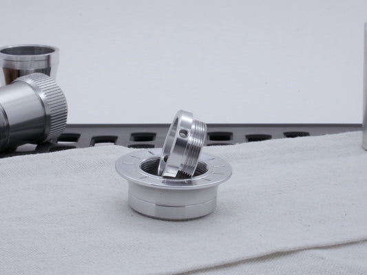 A basic, VHC-compatible, lightsaber Emitter Tip resting upon a lightsaber Emitter Flange, on cloth among other parts.