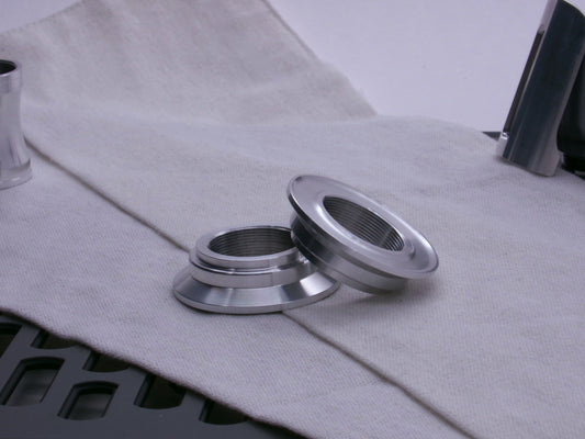 A pair of aluminum, VHC compatible, lightsaber emitter flanges resting askew on a coarse cloth.