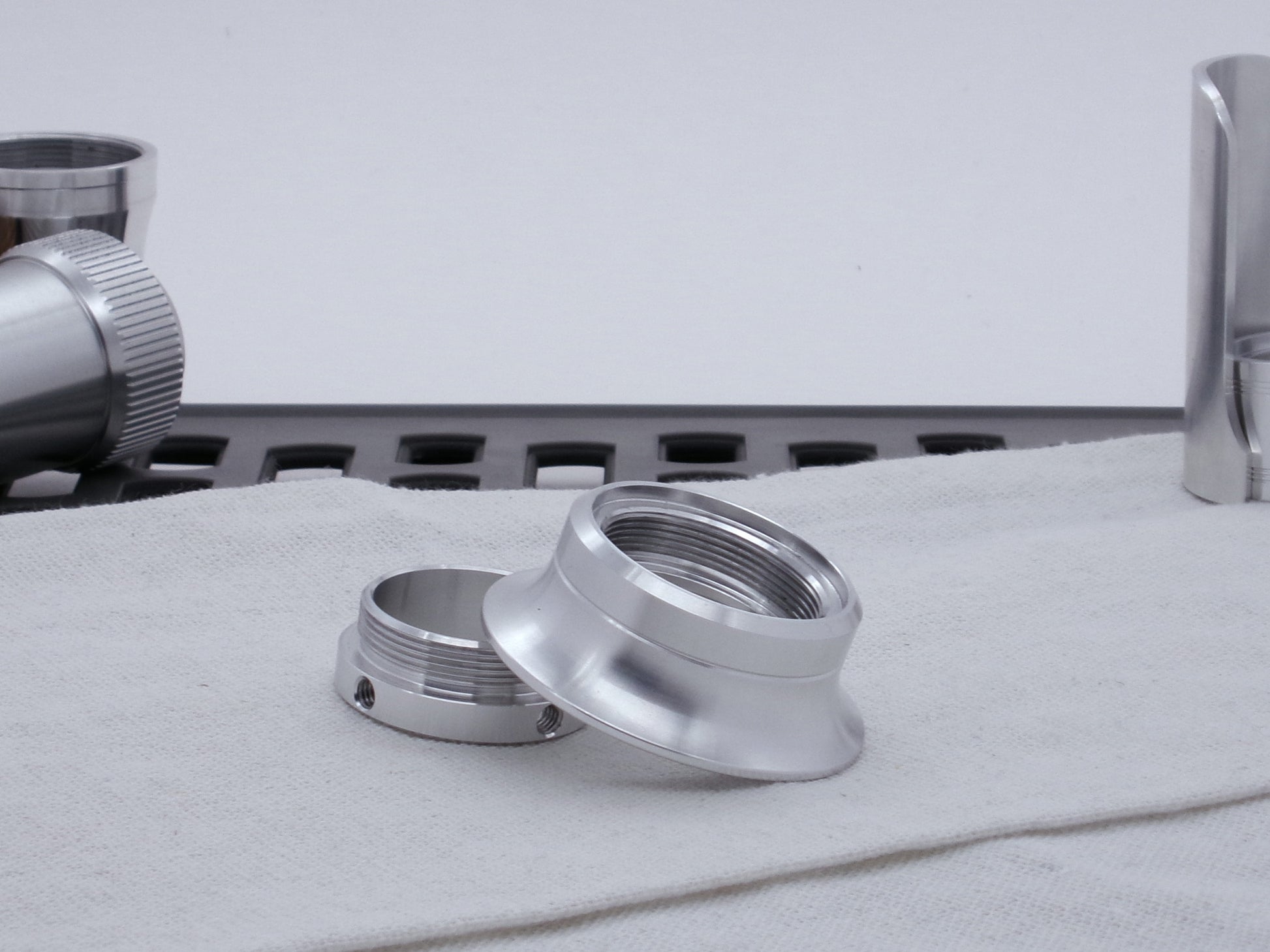 A VHC compatible lightsaber Emitter Flange askew and upside down atop an Emitter Tip in profile, resting on cloth among lightsaber parts.