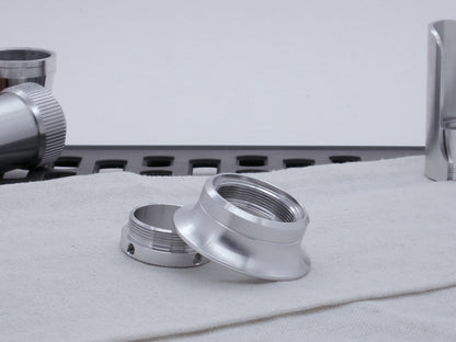 A VHC compatible lightsaber Emitter Flange askew and upside down atop an Emitter Tip in profile, resting on cloth among lightsaber parts.