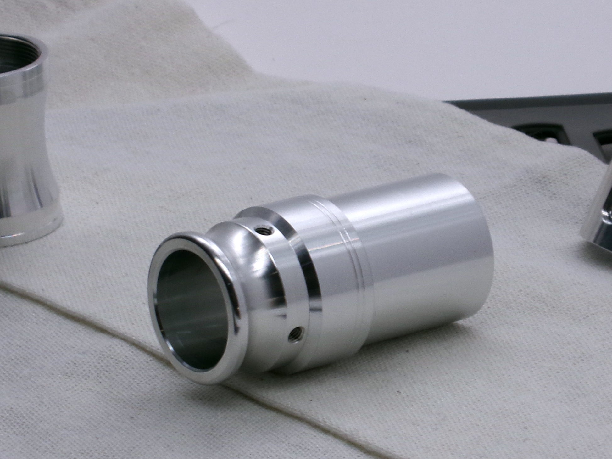 An aluminum, VHC compatible emitter tip installed on several lightsaber components, 3/4 view on a coarse cloth.