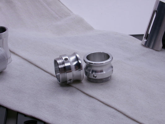 A pair of aluminum male-threaded emitter tips resting askew on a coarse cloth.