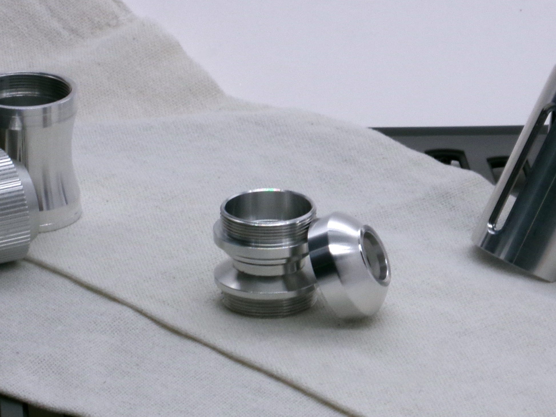A basic, aluminum female-threaded pommel leaning against the Adapter MM Hybrid Type 1 showing rounded profile and sound aperture.